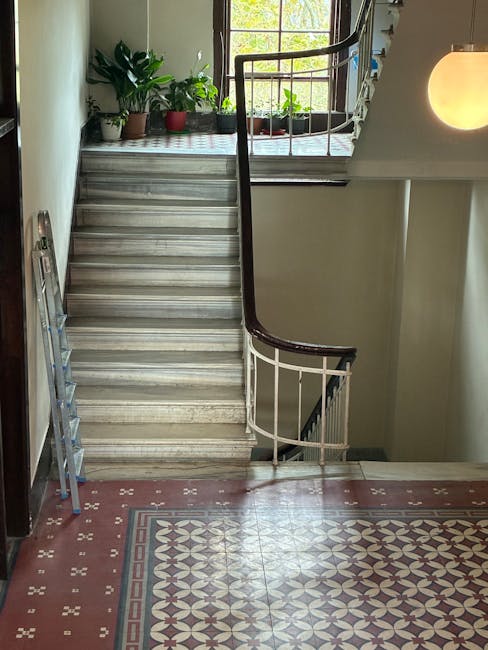 A set of indoor stairs leading up to an upper level in a building, constructed with metal and painted with yellow safety rails along both sides. The stairs have black and yellow anti-slip strips on each step and a sign in the middle reading 'PLEASE KEEP LEFT'. Surrounding the staircase is industrial scaffolding and metal framework, indicating a construction or renovation environment. The area is lit with artificial lighting, highlighting the sturdy structure used for home relocation or furniture transport, consistent with staircase and lift solutions discussed in Golders Green house removals services by Man with Van Golders Green. The scene captures the typical movement and logistical setup for loading or unloading furniture during a professional house move.