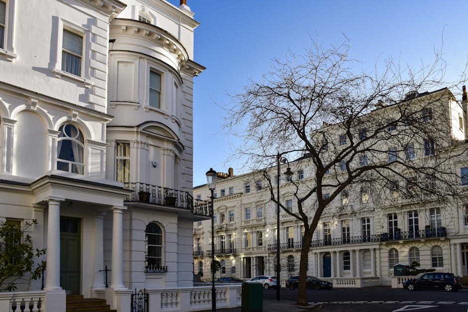 Photograph of a residential street in Golders Green showing white Edwardian-style terraced houses with ornate architectural details, large windows, and decorative balconies. In the foreground, there a